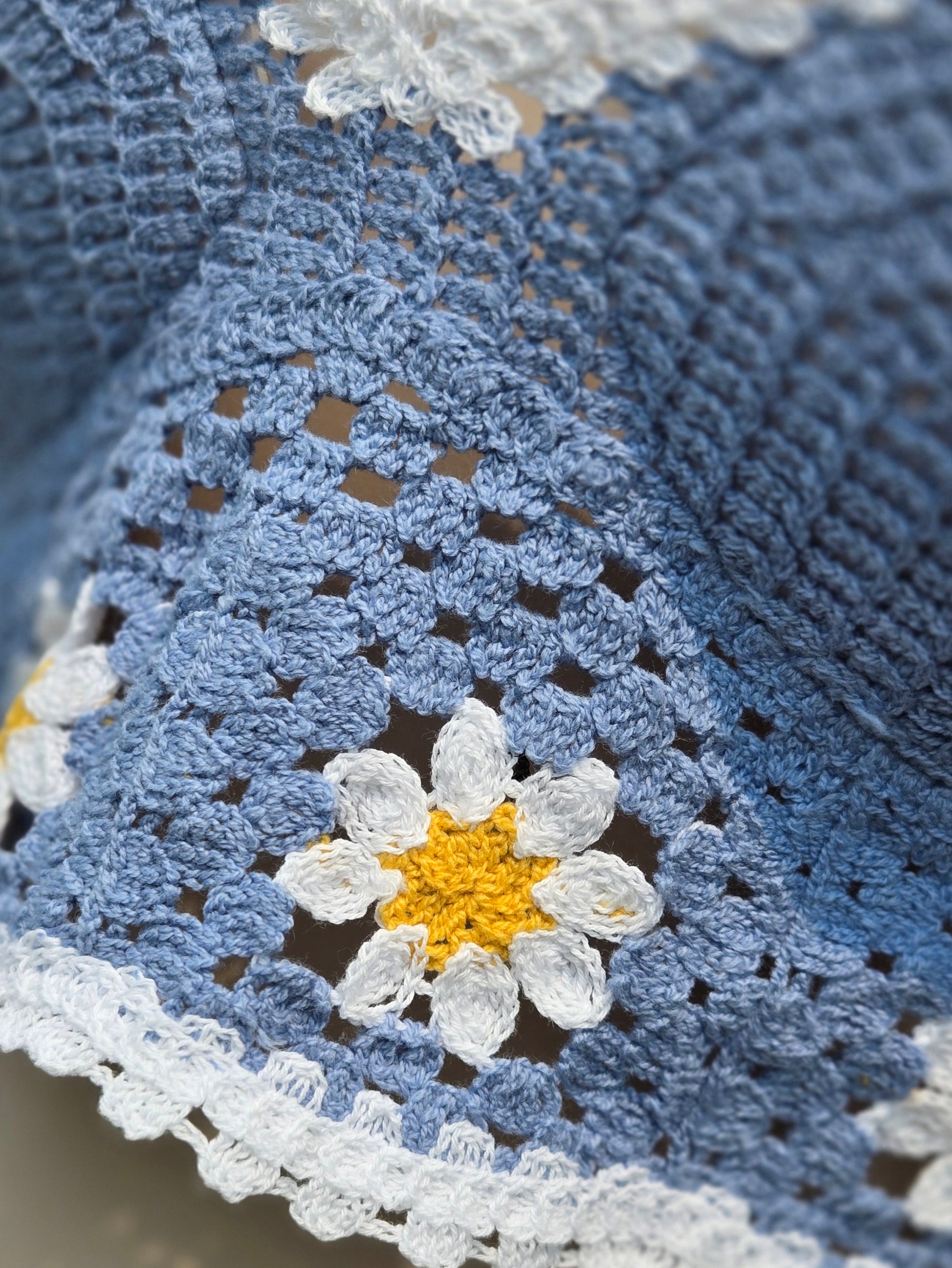 Close-up of a blue crochet halter top with a white daisy flower design.