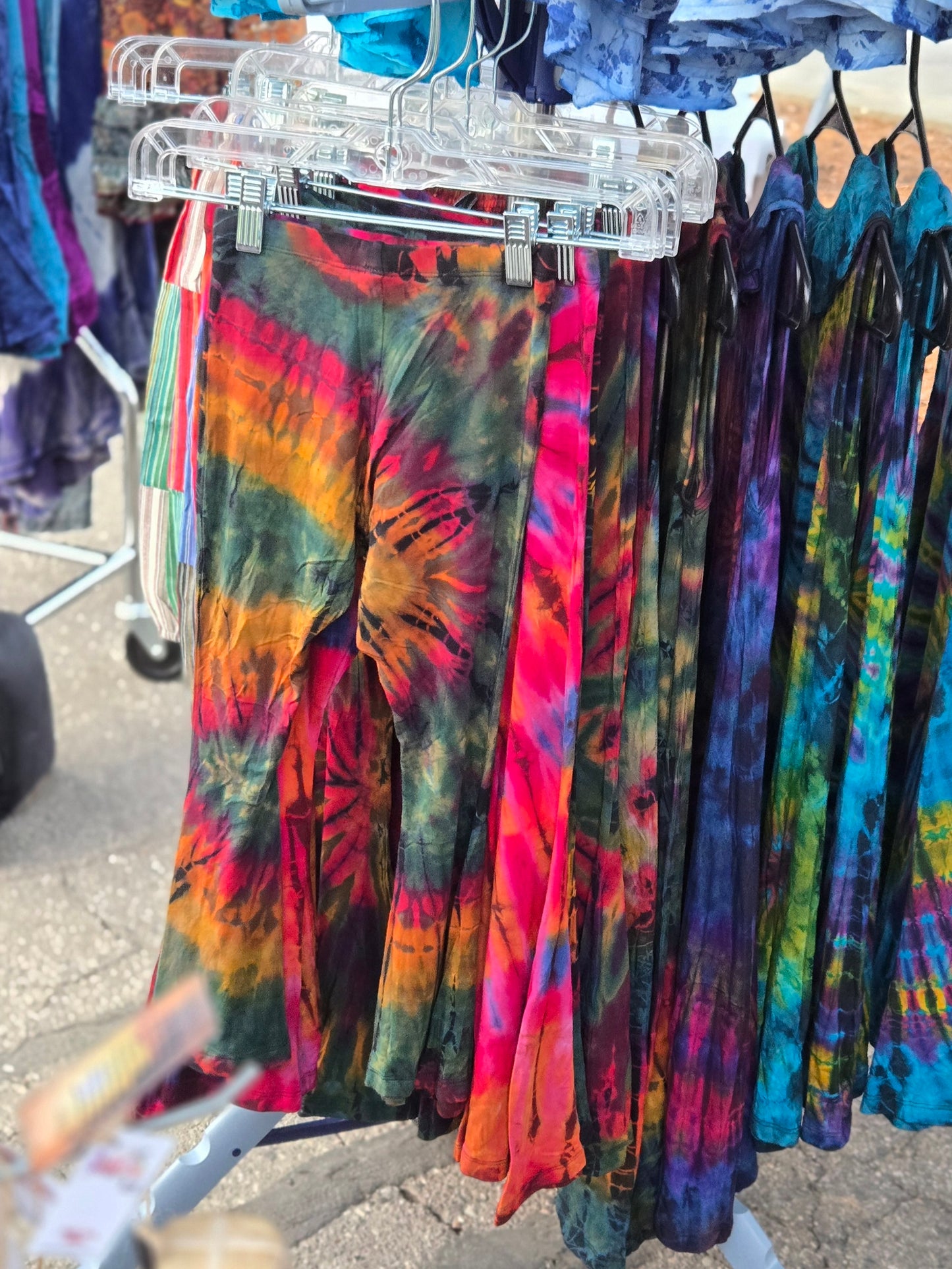 Colorful kids tie-dye bell bottom pants hanging on a rack outdoors.