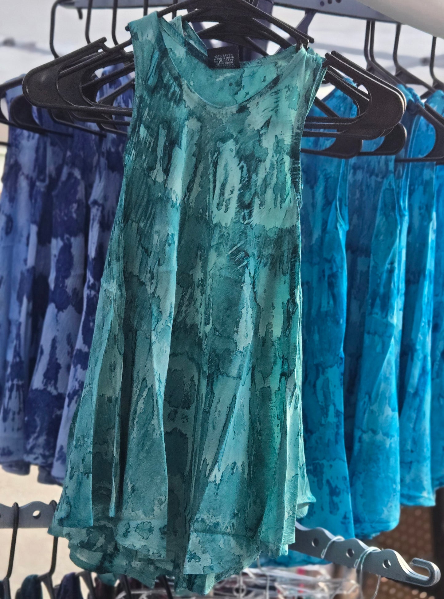 Teal girls tie dye dress on a rack with blue patterned items in the background