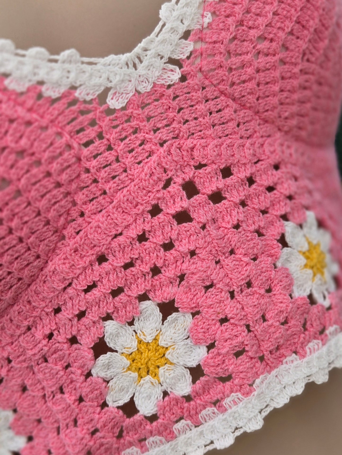 Close-up of a pink crochet halter top with white border and daisy flower patterns.