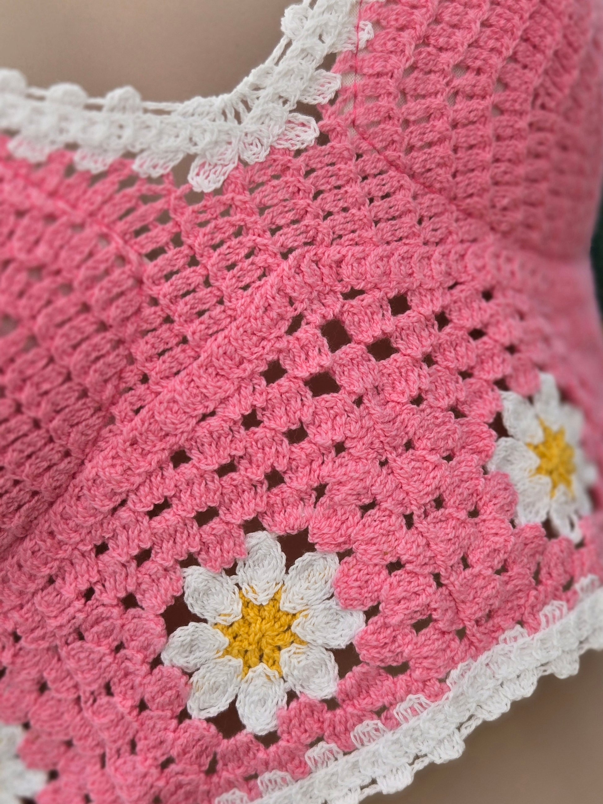 Close-up of a pink crochet halter top with white border and daisy flower patterns.