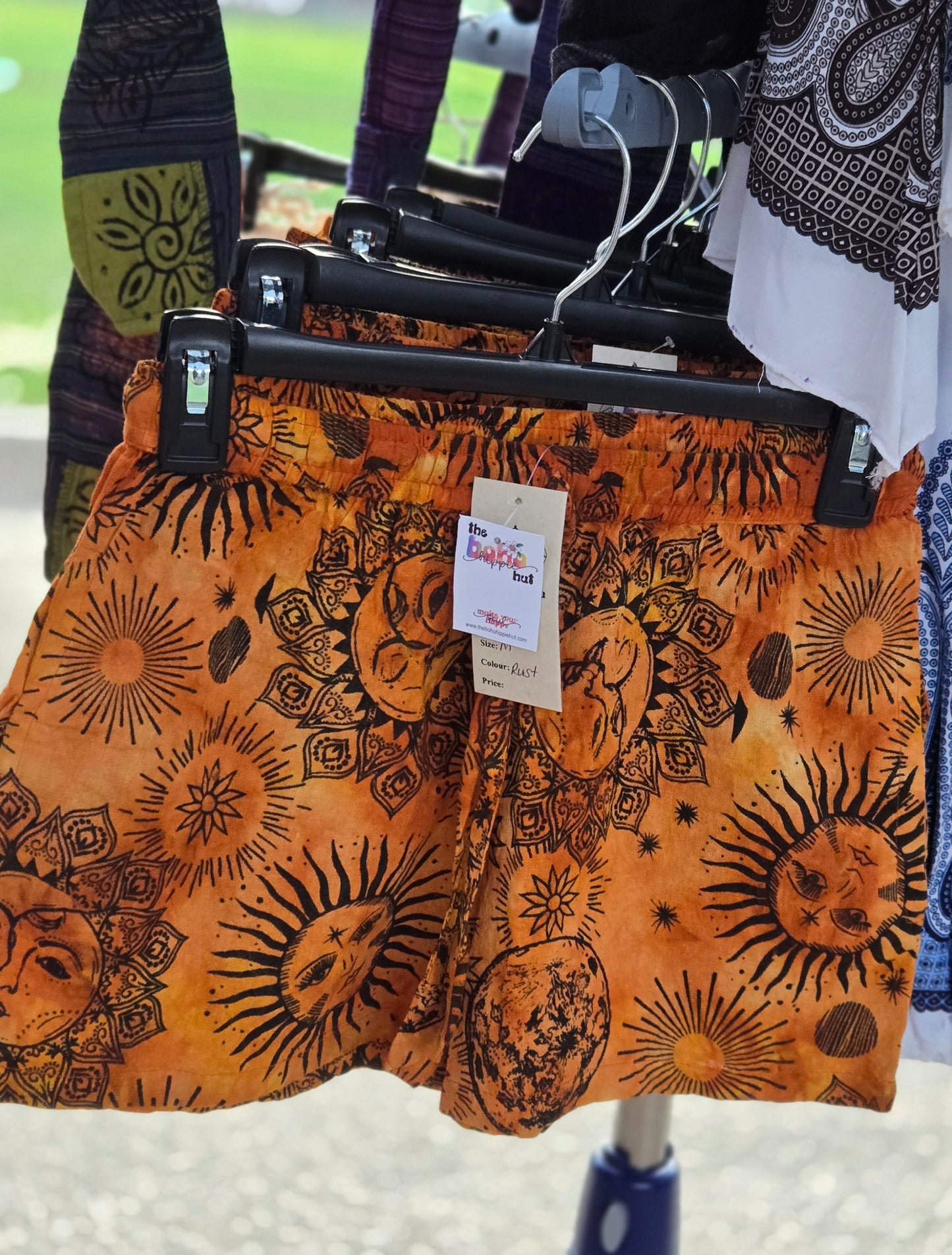 Orange shorts with black sun and moon patterns on a hanger with a tag.