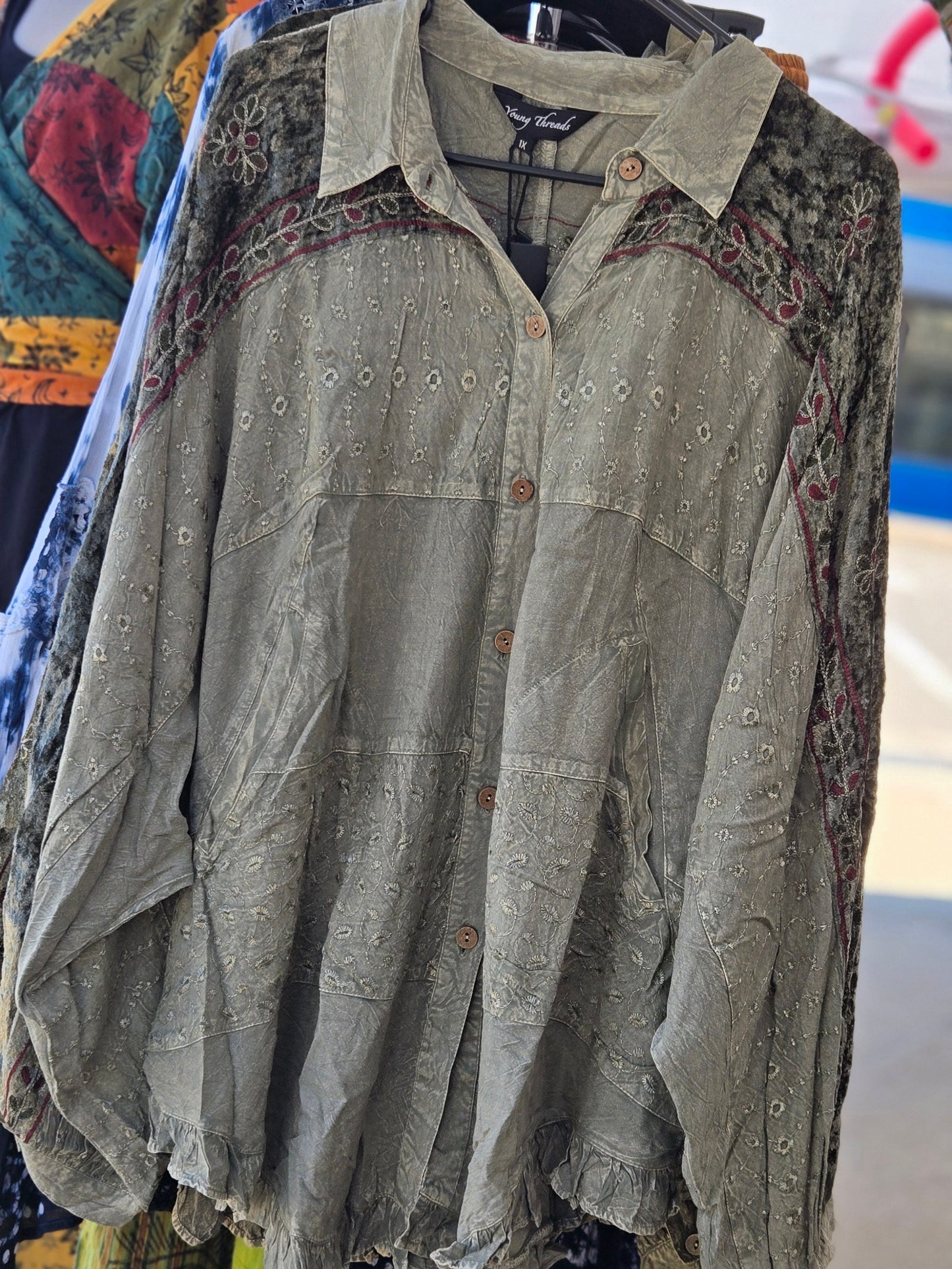 Green embroidered blouse on a hanger with colorful fabric in the background