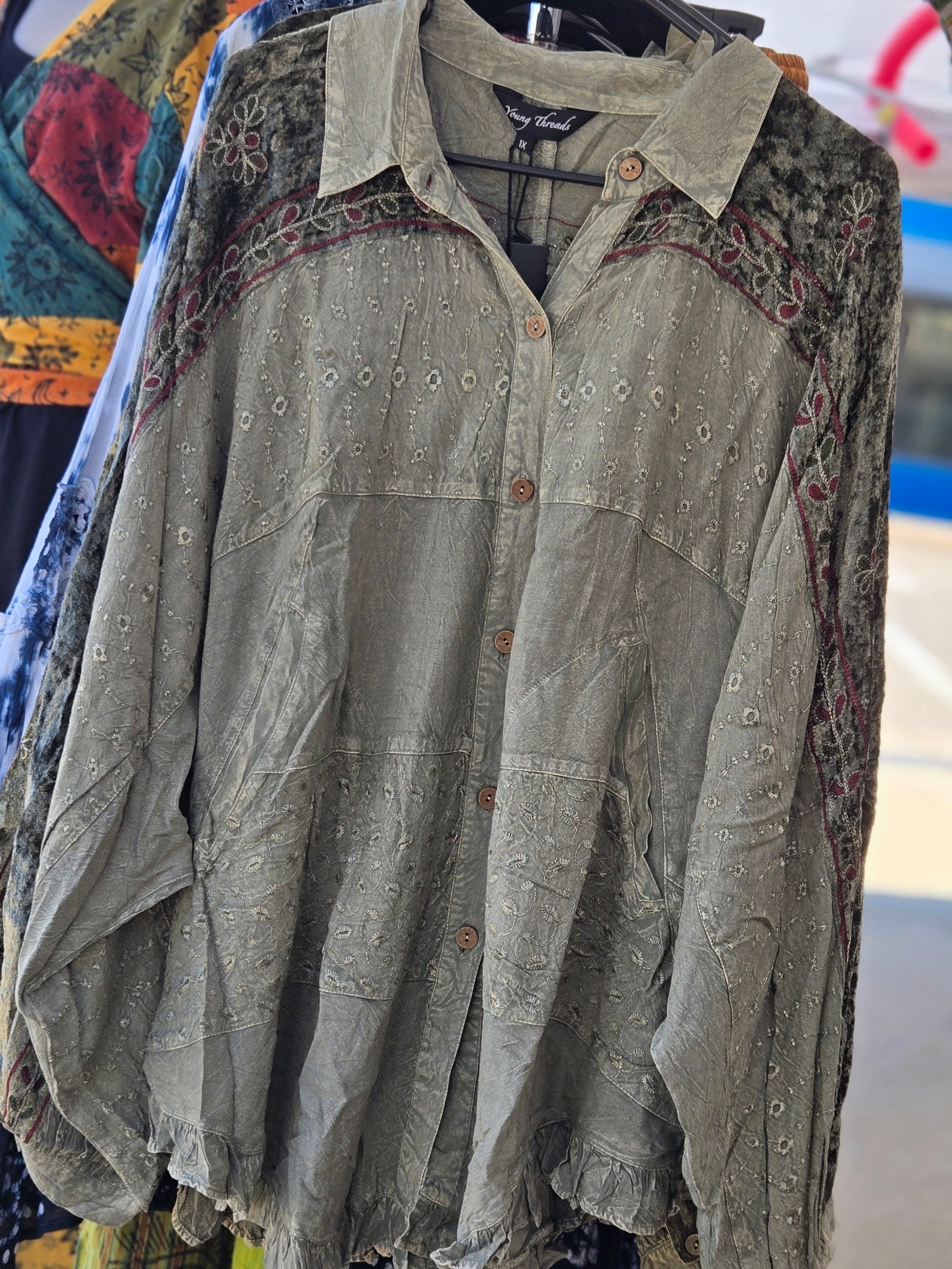 Green embroidered blouse on a hanger with colorful fabric in the background