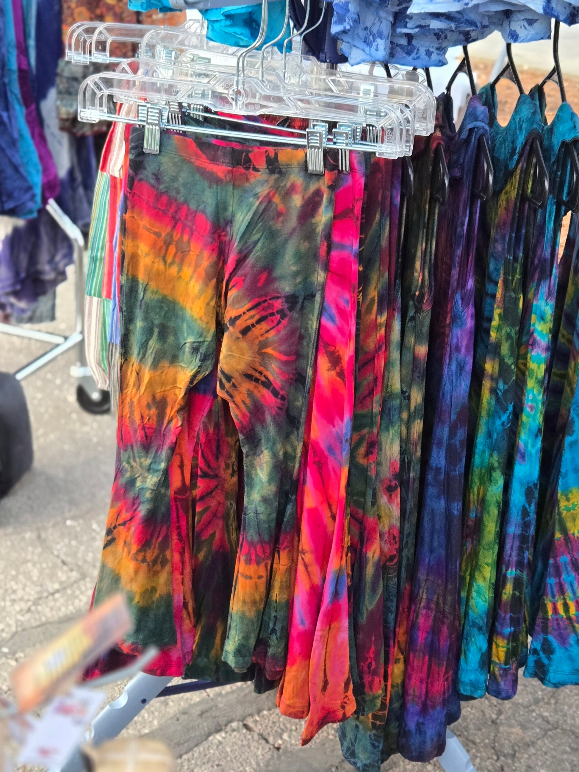 Colorful kids tie-dye bell bottom pants hanging on a rack outdoors.