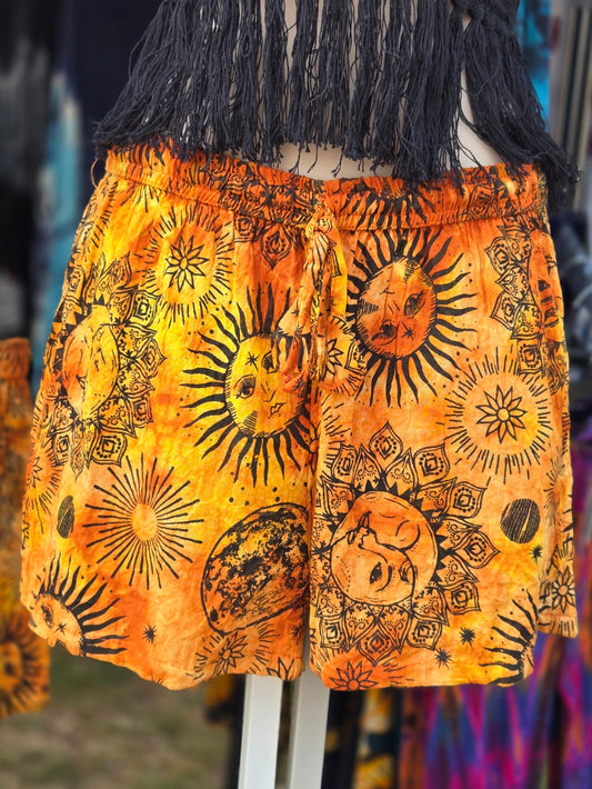 Orange shorts with black sun and moon patterns on a mannequin against a colorful background.