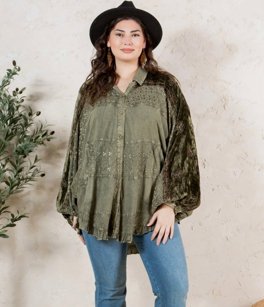 Woman wearing a green patterned blouse and black hat against a beige wall.