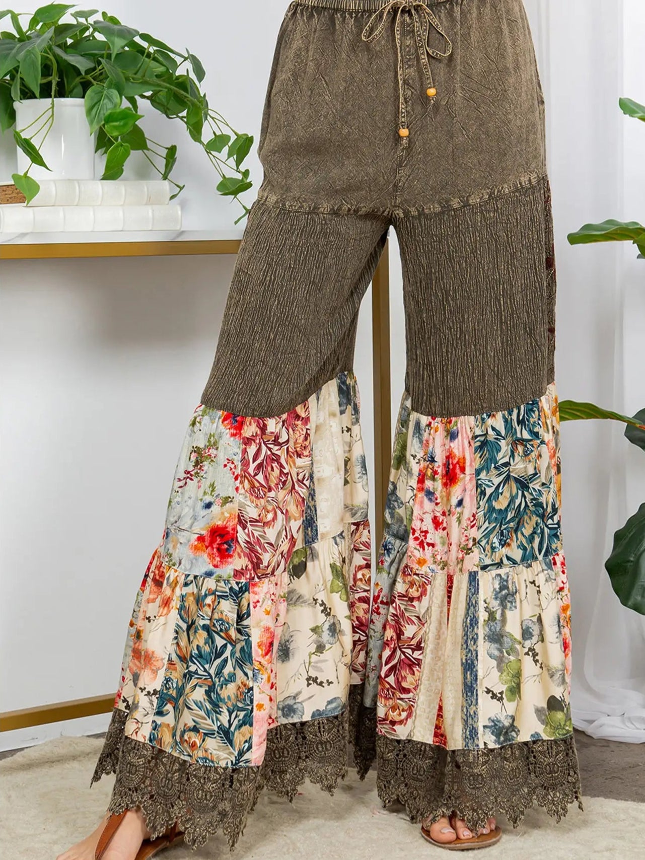 Brown wide-leg pants with floral patchwork at the bottom worn by a person indoors.