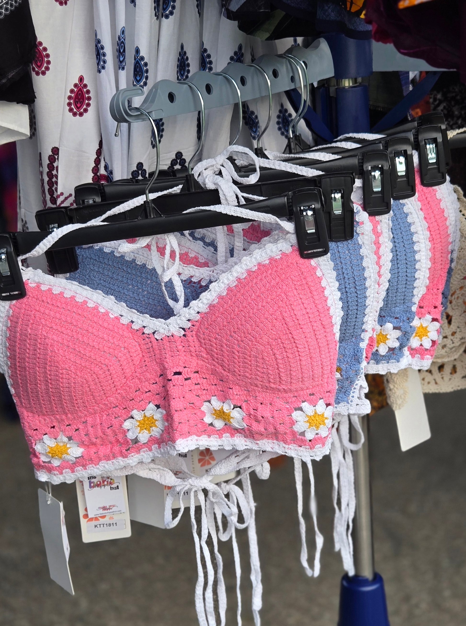 Pink crochet halter top with white flowers on a hanger with other clothing items.