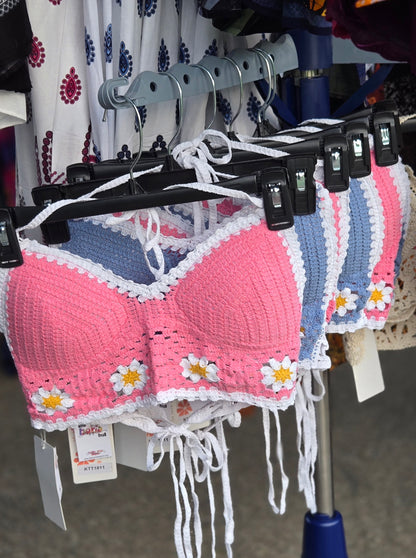 Pink crochet halter top with white flowers on a hanger with other clothing items.
