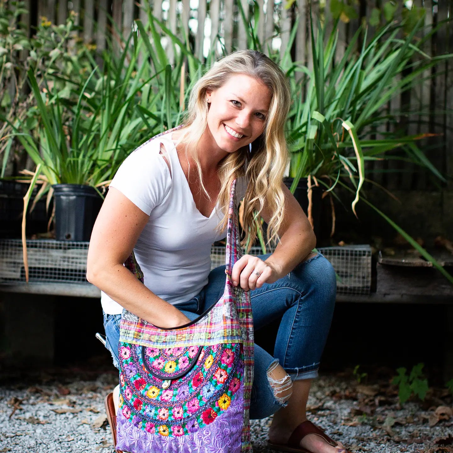 Woman holding a colorful hobo bag in an outdoor setting with plants.