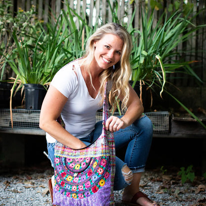 Woman holding a colorful hobo bag in an outdoor setting with plants.