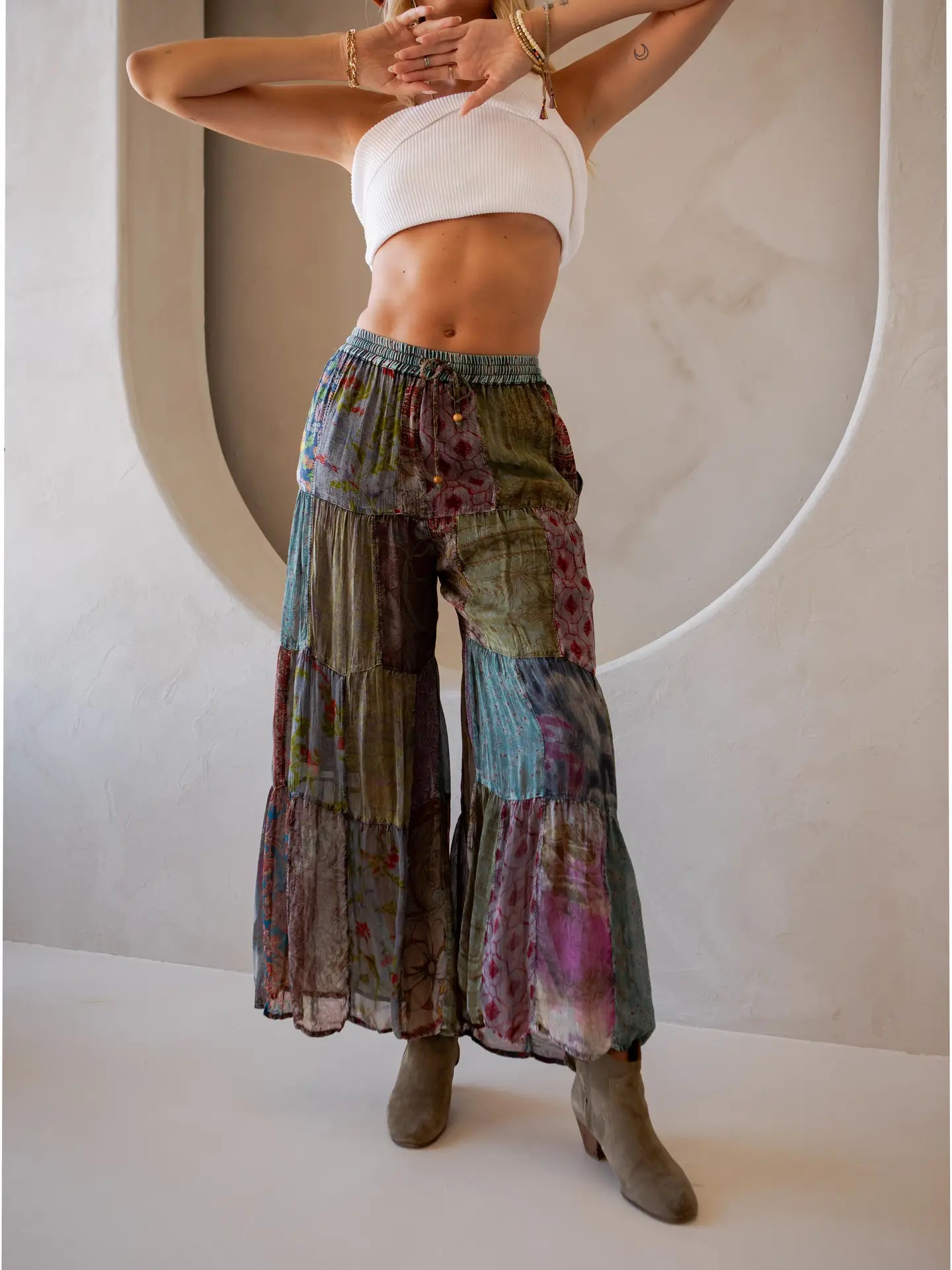 Woman wearing colorful tiered pants and a white top against a neutral background
