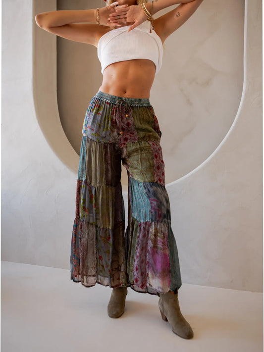 Woman wearing colorful tiered pants and a white top against a neutral background